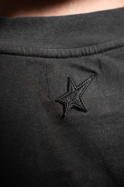 Close-up of a black cotton Tee with an embroidered black star logo on the chest.