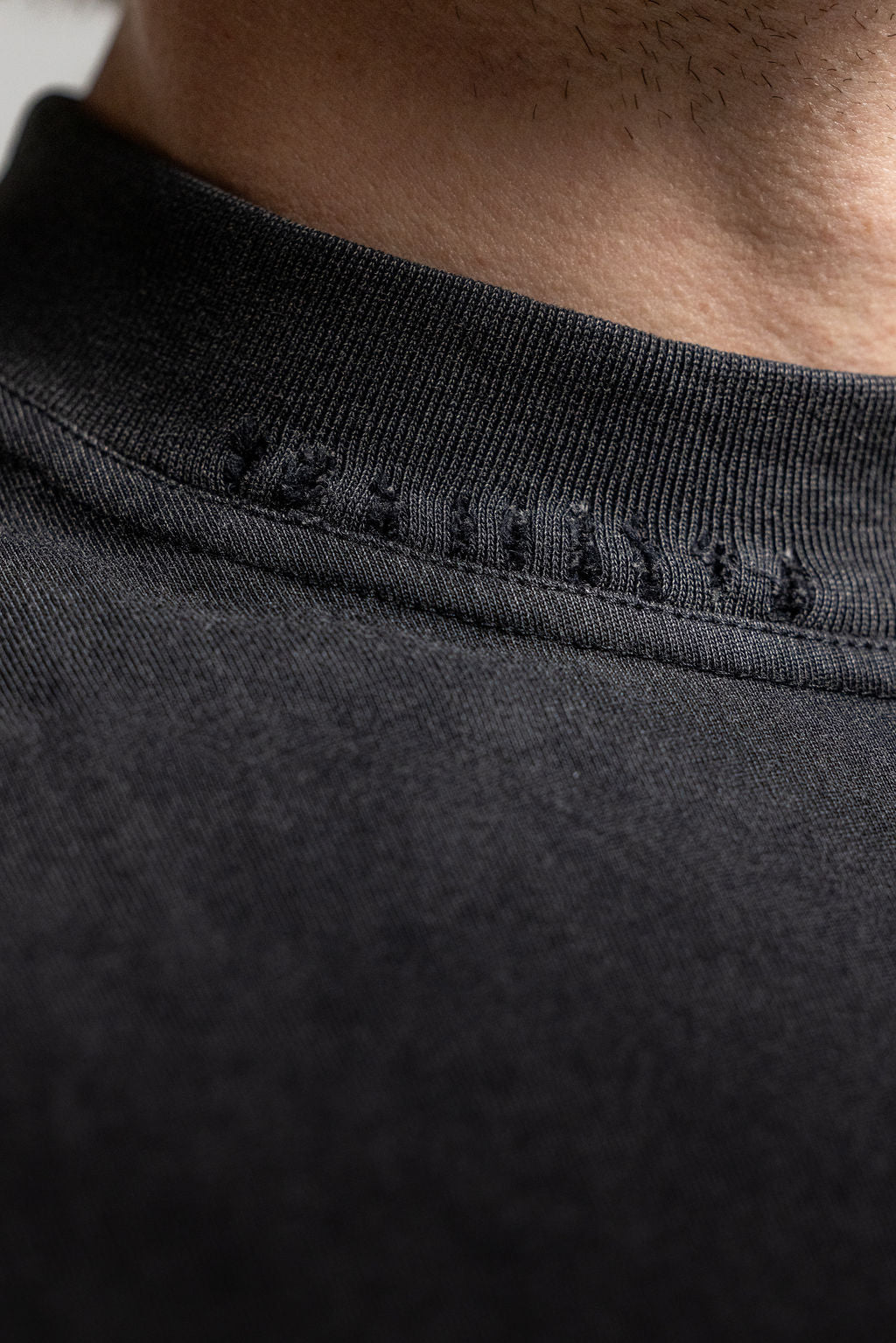 Close-up detail of a black crewneck t-shirt showing the ribbed collar and distressed detailing.