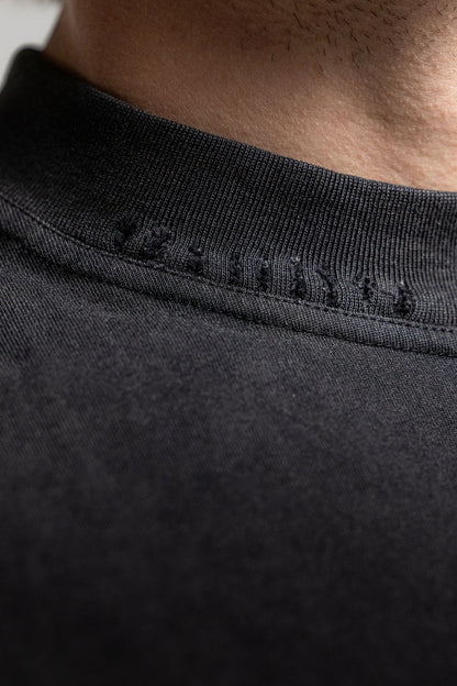 Close-up detail of a black crewneck t-shirt showing the ribbed collar and distressed detailing.