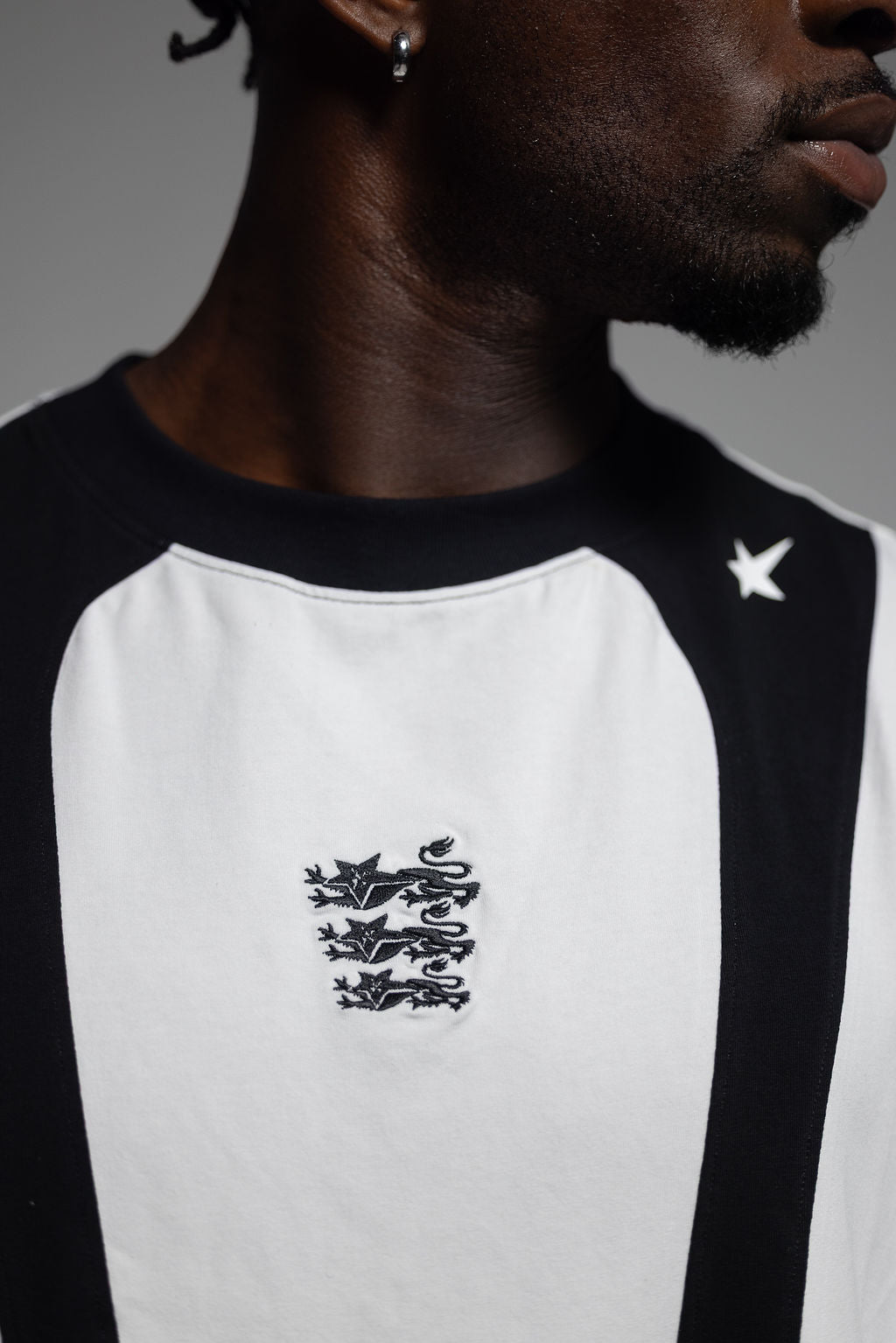 Close-up of a person wearing a black and white training singlet with a black embroidered England lion crest on the chest and a white star logo on the shoulder.