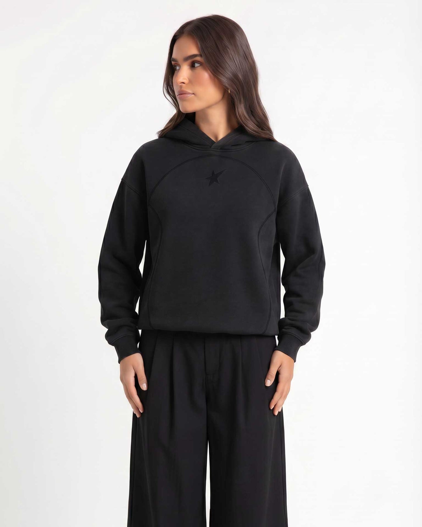 A woman modeling Trew Collections back on Black Hoodie, paired with black wide-leg sweatpants, against a plain light gray studio background.