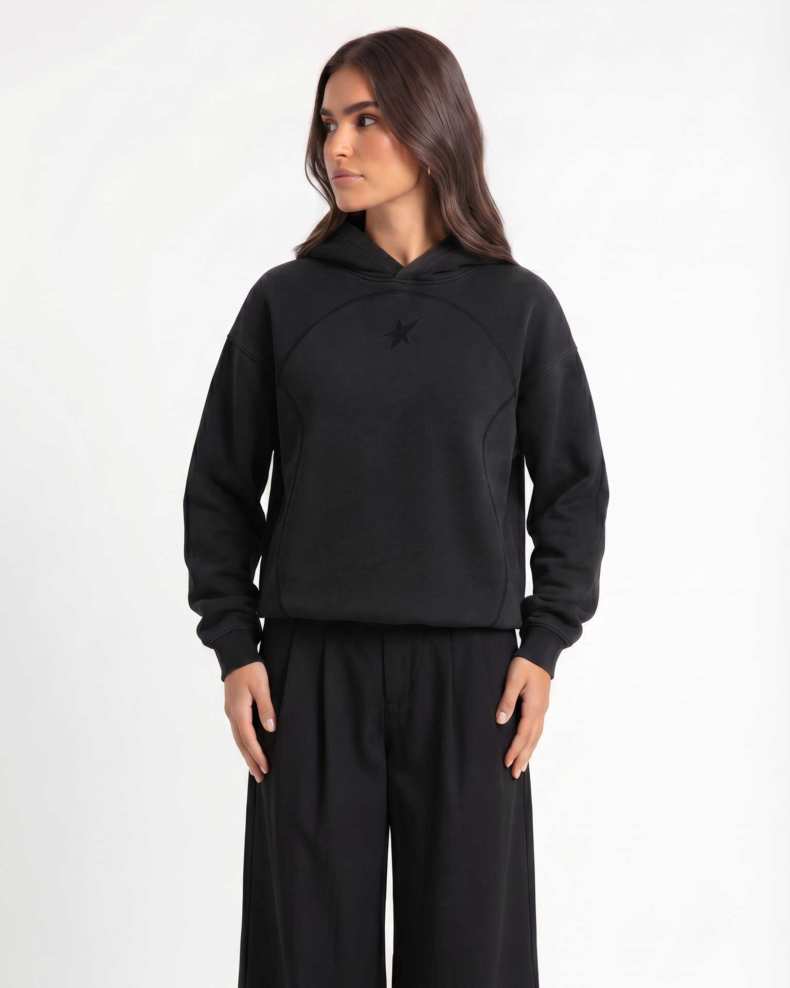 A woman modeling Trew Collections back on Black Hoodie, paired with black wide-leg sweatpants, against a plain light gray studio background.