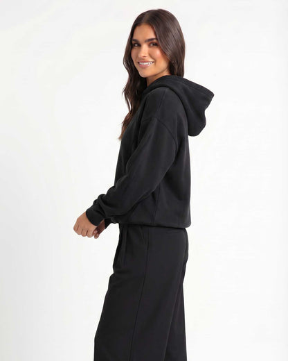 A woman modeling Trew Collections Black on Black hooded sweatshirt against a plain white studio background.